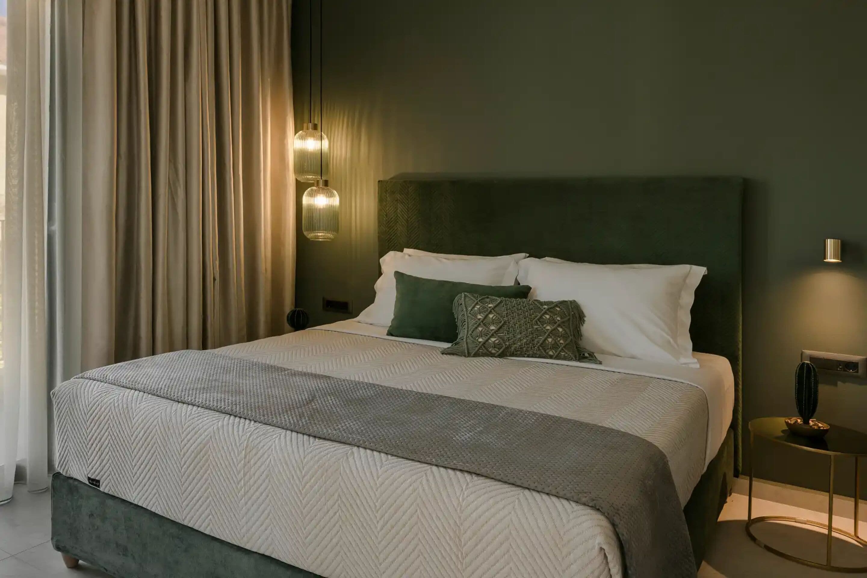 Una cama bien hecha con una colcha estampada, dos lámparas de noche y una mesita con un objeto decorativo.