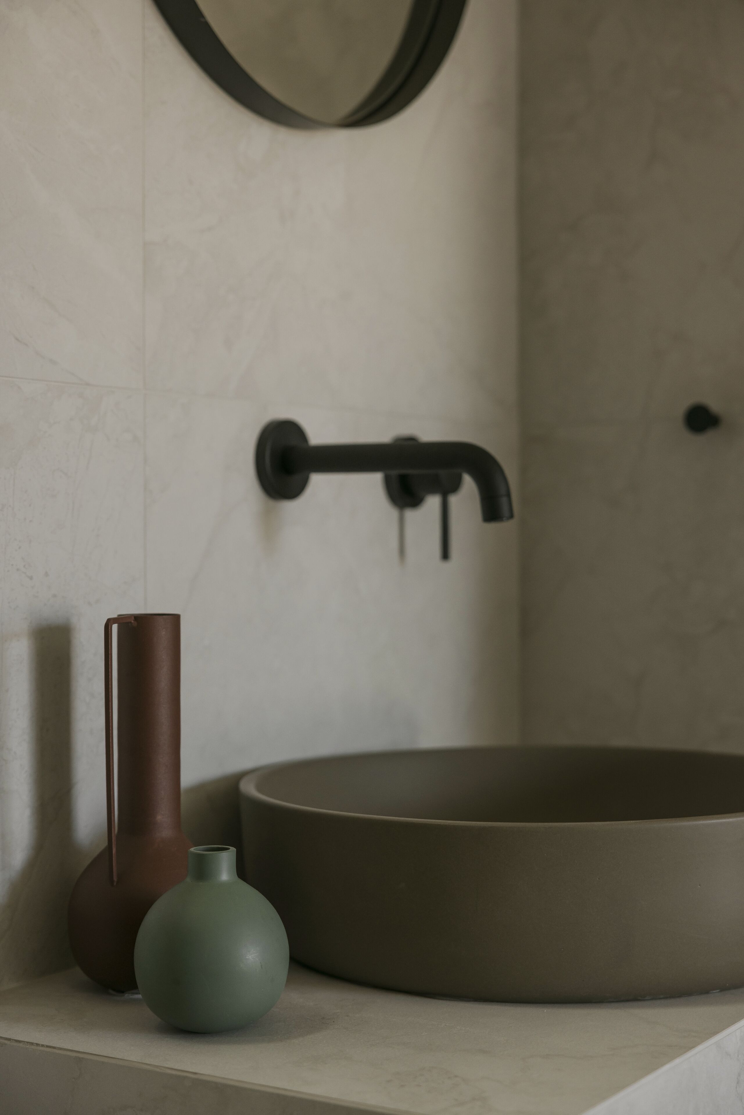 A bathroom with a round sink, a tall vase, and a mirror on the wall.