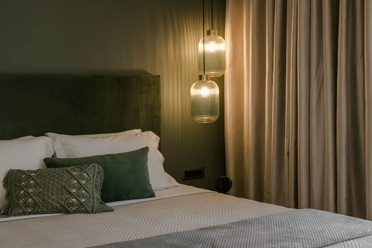 Cama bem arrumada com almofadas brancas e verdes, cabeceira verde e duas luminárias pendentes.