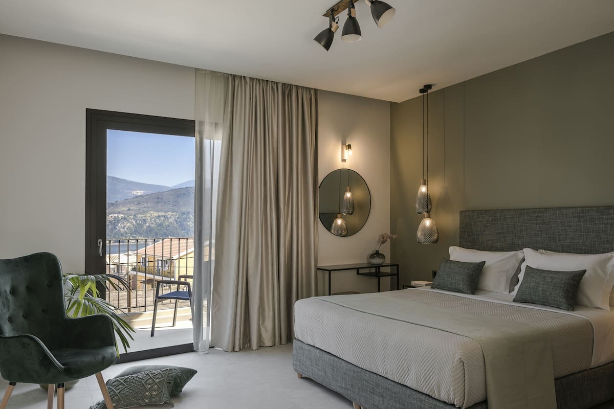 Quarto com cama grande, uma cadeira, uma escrivaninha e vista para o exterior.