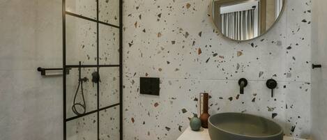 A modern bathroom with a glass shower enclosure, a large vessel sink, and a round mirror on the wall.
