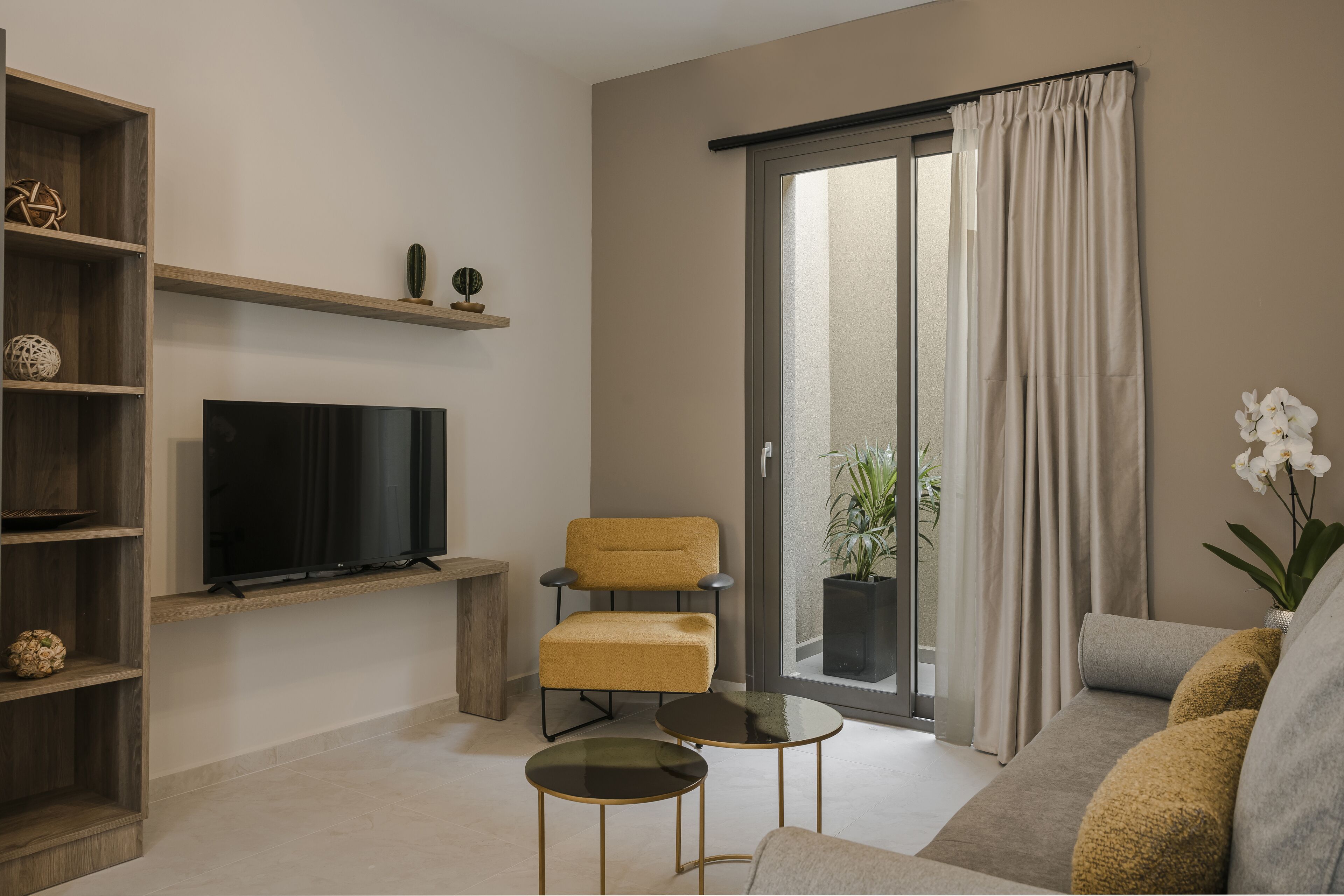 Una sala de estar moderna con un televisor de pantalla plana, un sillón amarillo, una mesa de centro de vidrio y un ventanal corredero que da a un balcón.