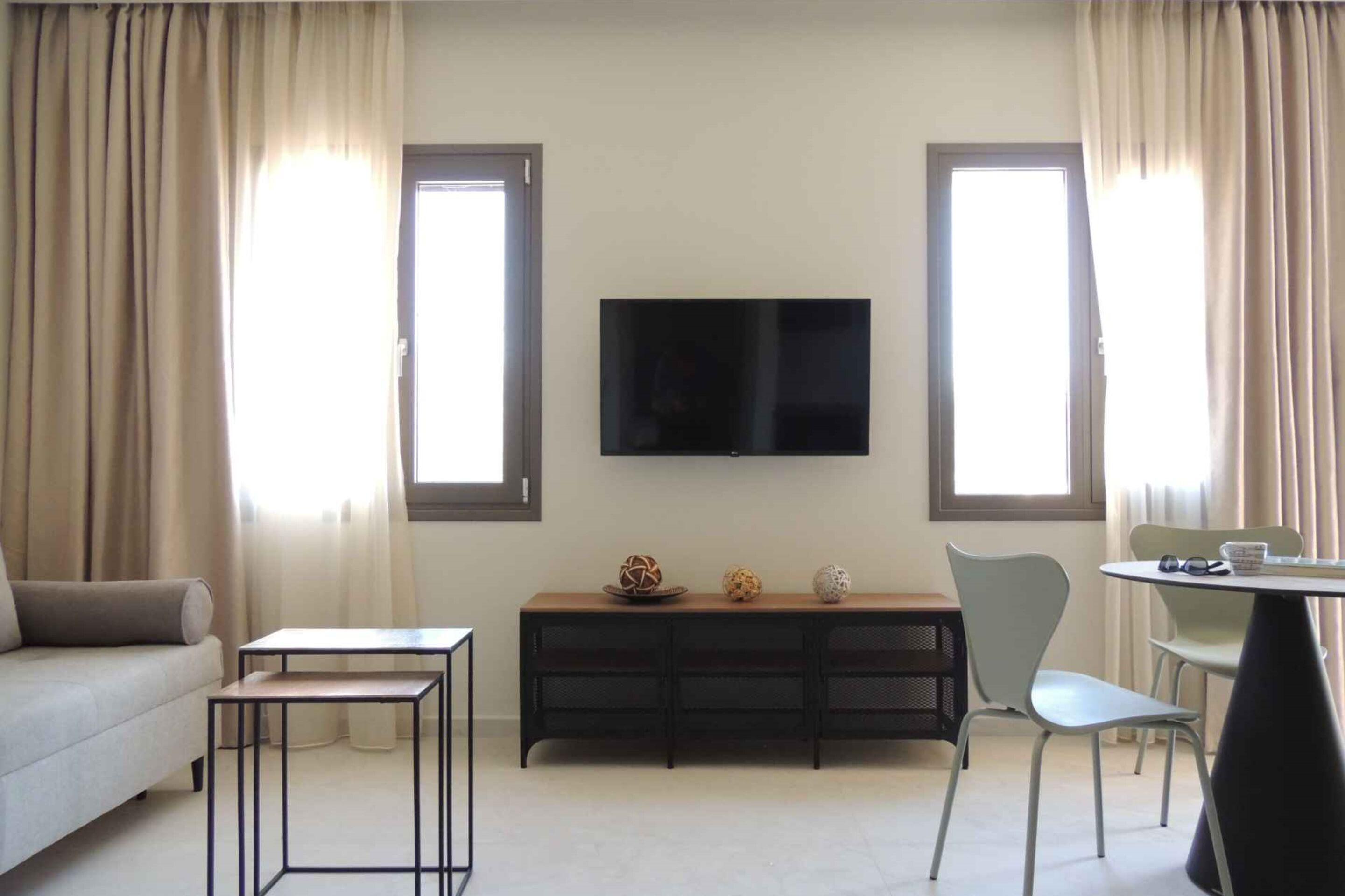 Ein modernes Wohnzimmer mit Sofa, Couchtisch, Fernseher und einem Essbereich mit Stühlen.
