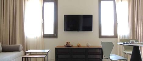 Ein modernes Wohnzimmer mit Sofa, Couchtisch, Fernseher und einem Essbereich mit Stühlen.