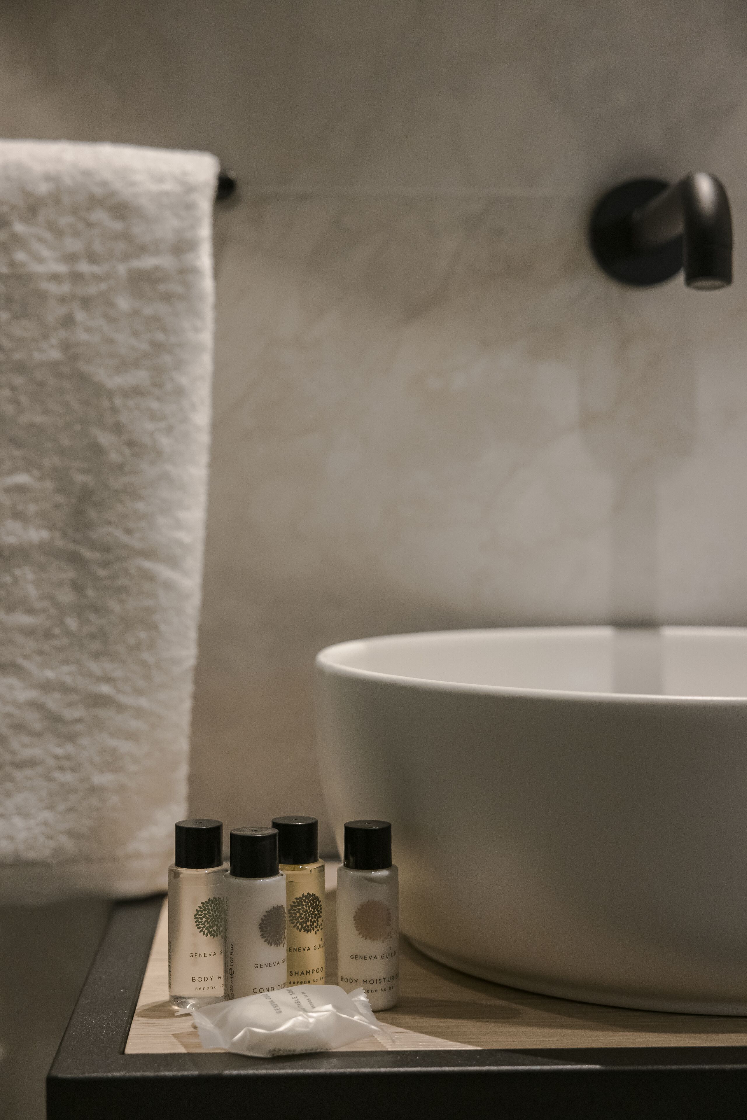 A bathroom with a white sink, a towel, and several bottles of body care products.