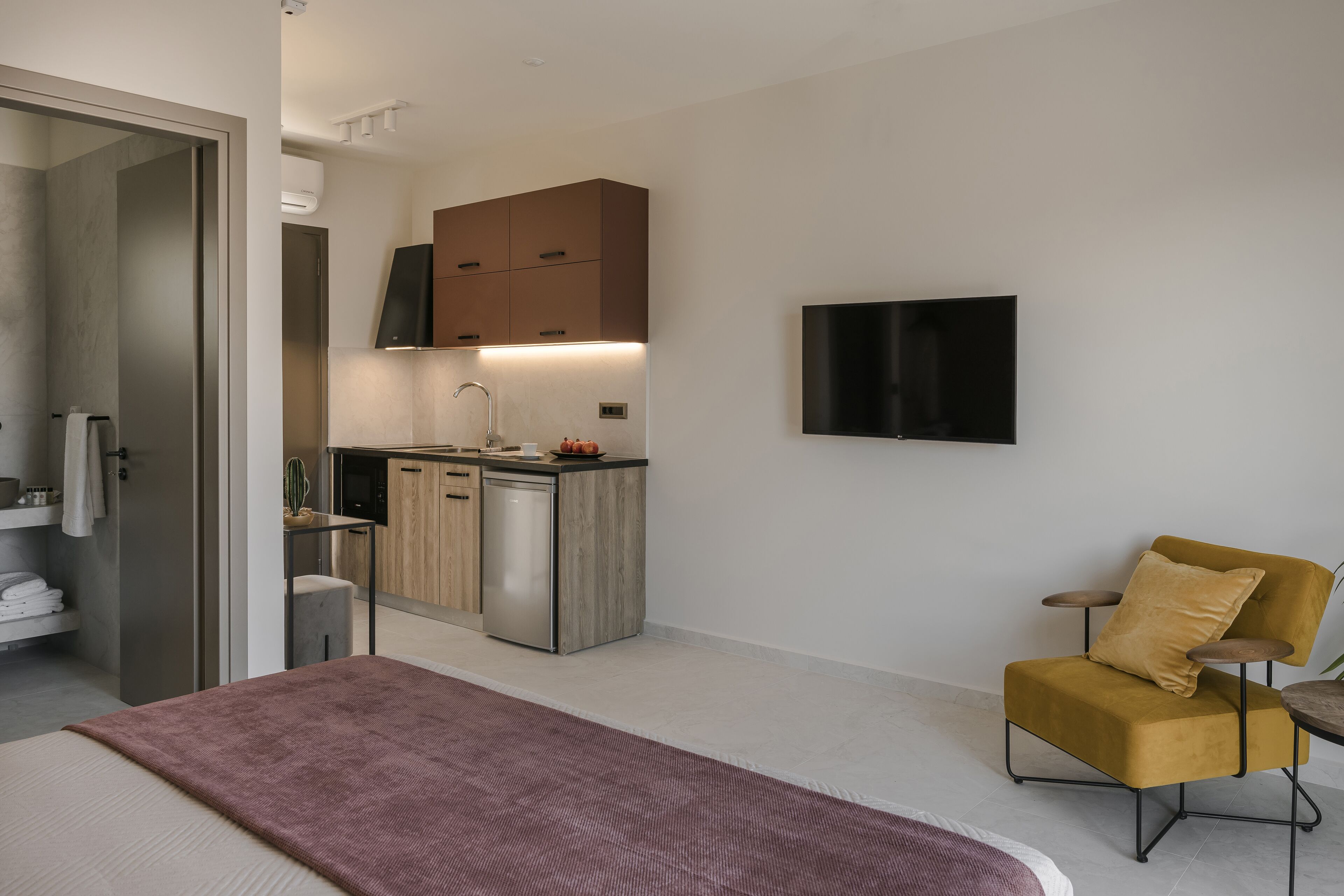 Ett modernt hotellrum med en säng, ett litet skrivbord, en stol, en TV och ett litet pentry.