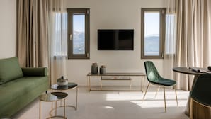 Un salon moderne avec un canapé vert, une table ronde, un fauteuil vert, un téléviseur fixé au mur et une vue sur les montagnes par les fenêtres.