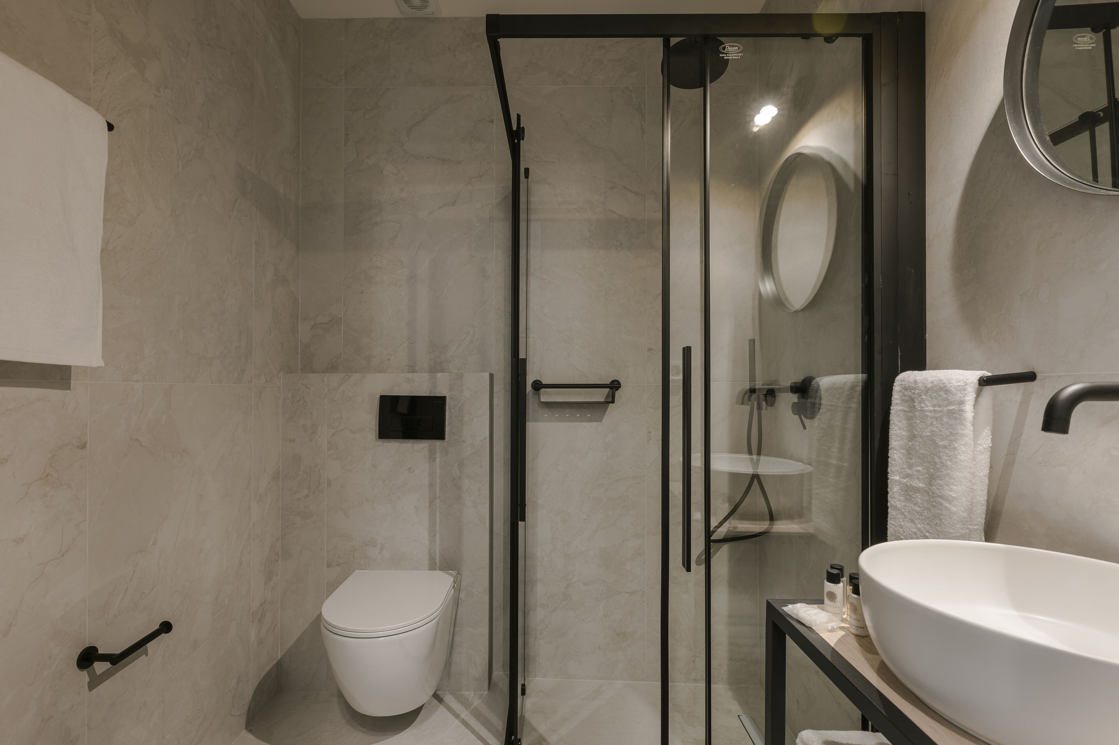 Un baño moderno con ducha de vidrio, inodoro blanco y un lavamanos grande con espejo superior.