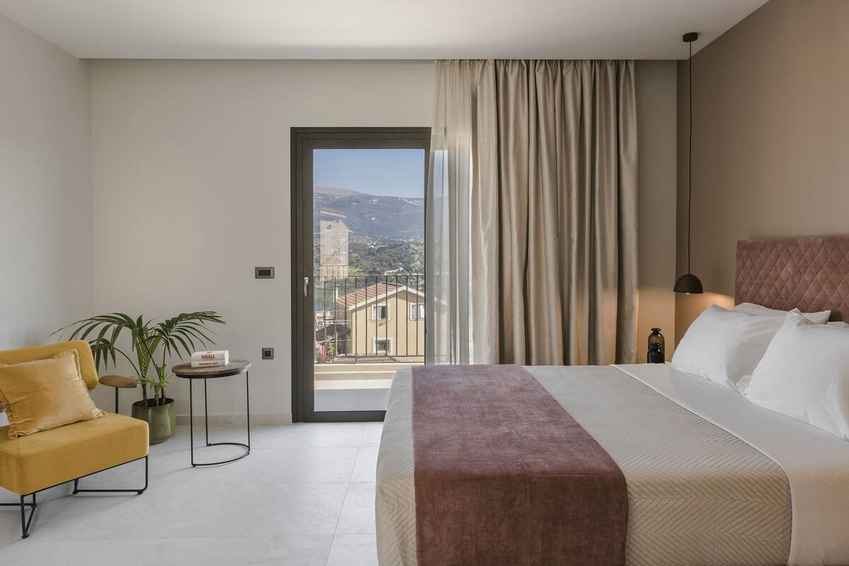 Quarto de hotel com uma cama grande, uma cadeira, uma mesinha e um vaso de planta.