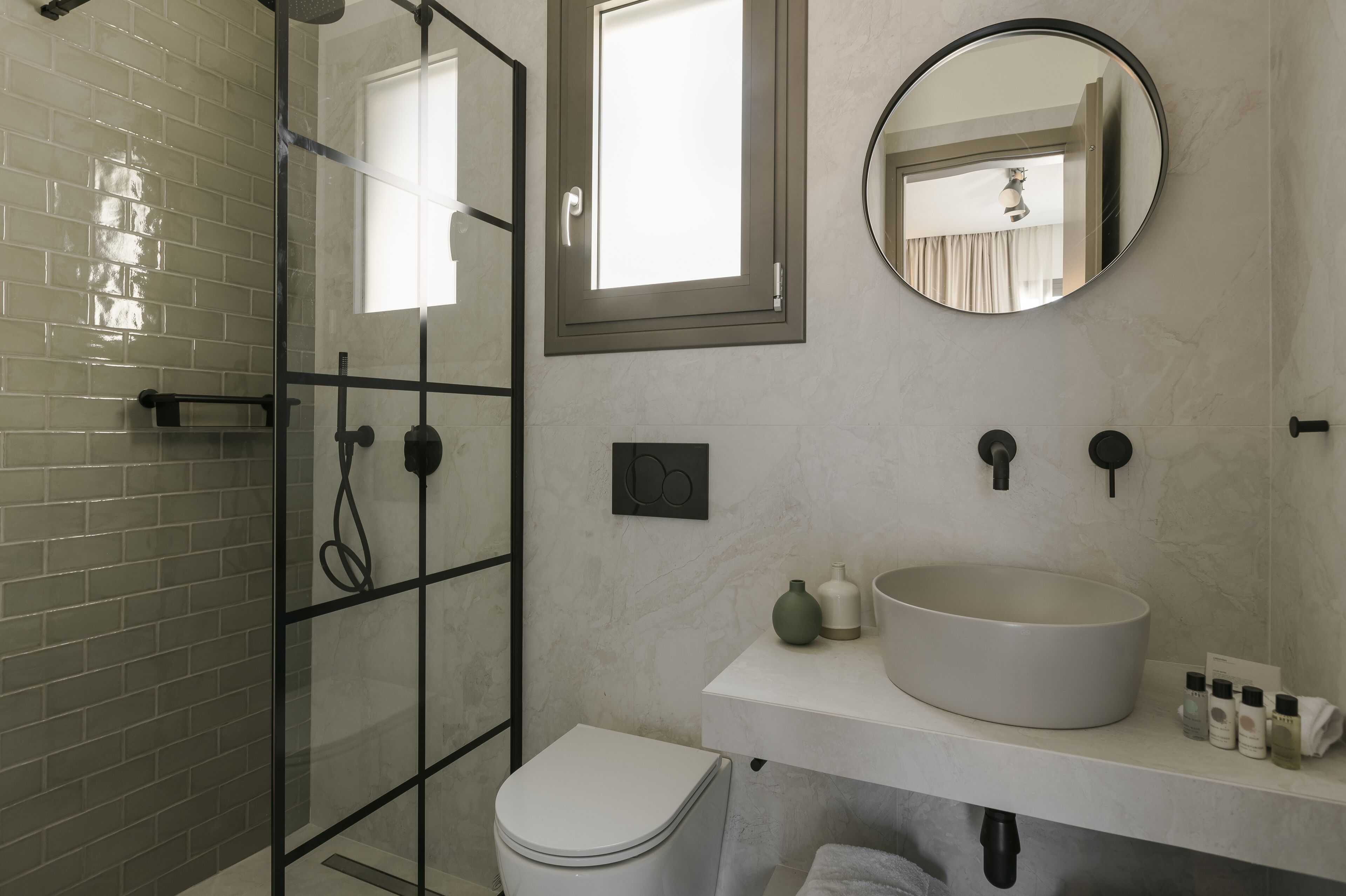 Un baño moderno con cabina de ducha de vidrio, un inodoro blanco, un lavabo grande y redondo, y un espejo sobre el lavabo.