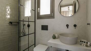 Un baño moderno con cabina de ducha de vidrio, un inodoro blanco, un lavabo grande y redondo, y un espejo sobre el lavabo.