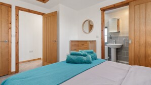 A bedroom with a bed, a wooden wardrobe, a dresser, a mirror, and a bathroom visible through an open door.