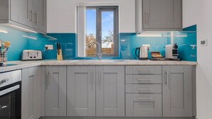 A modern kitchen with grey cabinets, a blue backsplash, a window with curtains, and a coffee machine.