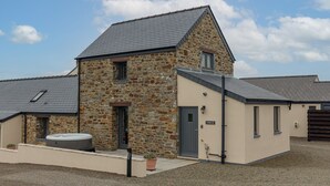 A stone building with a grey roof, a small porch, and a hot tub.