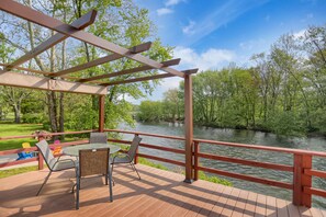 Een overdekt terras met een tafel en stoelen, met uitzicht op een rivier.