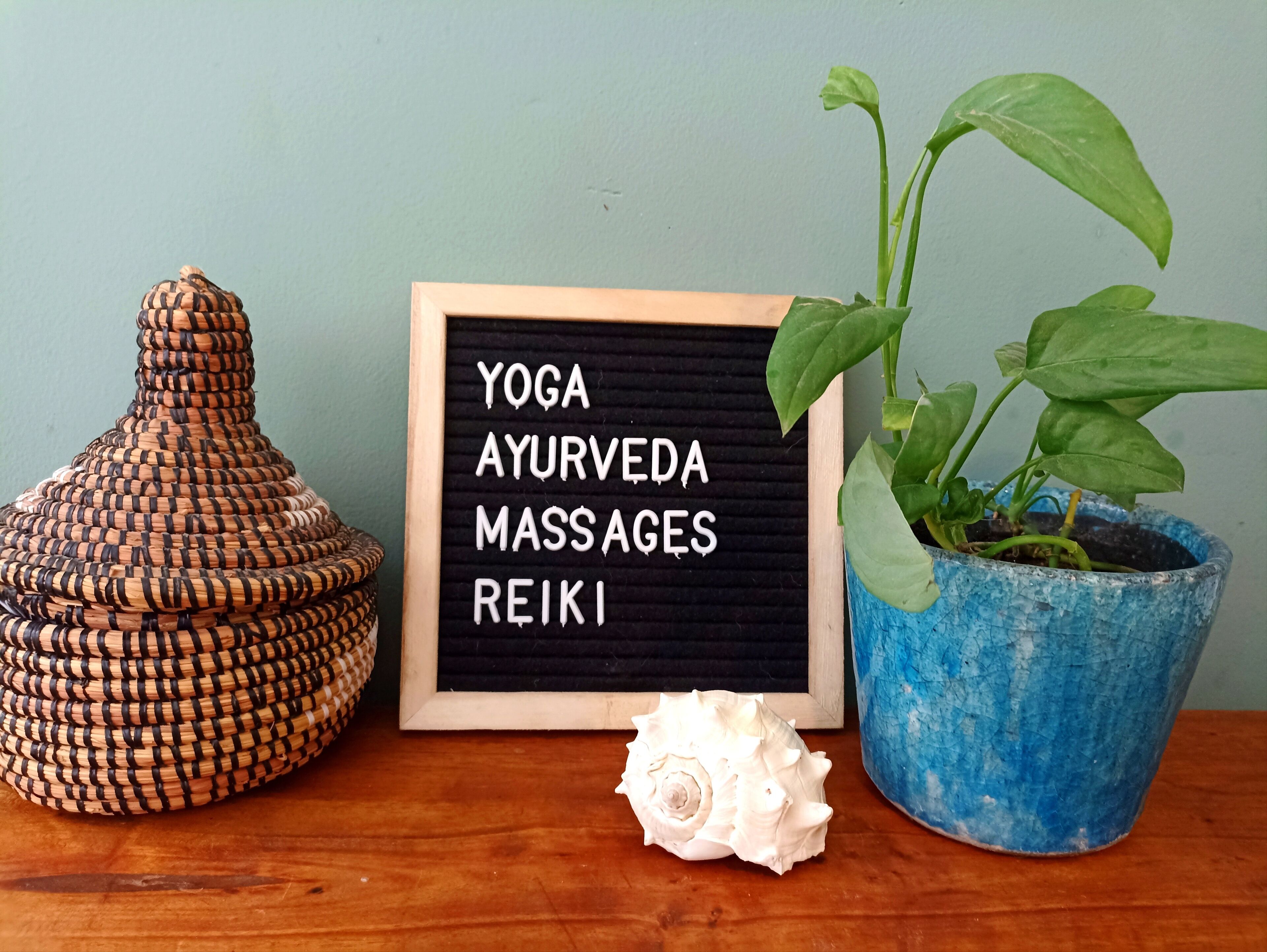 A wooden table with a blackboard displaying "YOGA, AYURVEDA, MASSAGES, REIKI" and a potted plant.