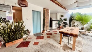 Un patio amplio con una mesa y sillas de madera, rodeado de plantas en macetas y una puerta azul.