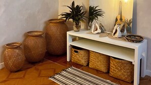 Una habitación con una consola blanca, cestos de mimbre, un tapete a rayas, un espejo grande y una lámpara colgante.