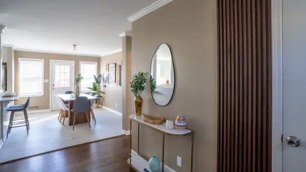 A spacious living area with a dining table, chairs, a console table with decorative items, and a large mirror.