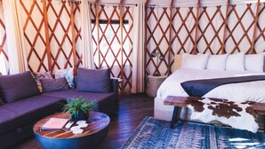 Ein gemütliches Zimmer mit einem Bett, einem Sofa, einem runden Holztisch und einem gemusterten Teppich.