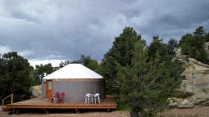 Ein Zelt mit Holzterrasse, zwei rote Adirondack-Stühle und ein weißer Stuhl.