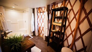 Ein Badezimmer mit Dusche, Waschbecken mit Pflanze, Holzregal und Handtuchhalter.