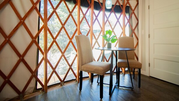 Ein Zimmer mit einer Holztrennwand, zwei Polsterstühlen, einem kleinen runden Tisch mit Blumentopf und einer weißen Tür.