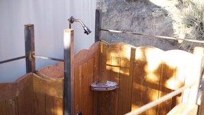 Une cabine de douche extérieure en bois, dotée d’un robinet en métal et d’un siège de douche.