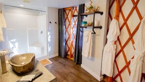 Une salle de bain avec un lavabo en pierre, un plancher en bois et un espace douche séparé par un claustra en bois.