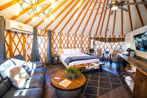 Una carpa espaciosa con una cama, un sofá, una mesa baja con una planta y una zona de comedor con sillas y una mesa.
