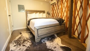Un dormitorio con estructura de cama de madera, ropa de cama blanca, alfombra mullida blanco y negro y un panel divisor de madera celosía.