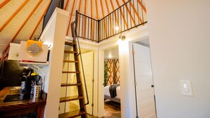 Un espacio tipo loft con una escalera de madera que da a una entreplanta. Se observa una zona de cocina a la izquierda, con varios electrodomésticos y utensilios.