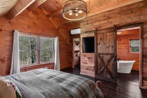 Eine Holzhütte mit Bett, großem Fenster, einer Schiebetür im Bauernhausstil und einer Badewanne.