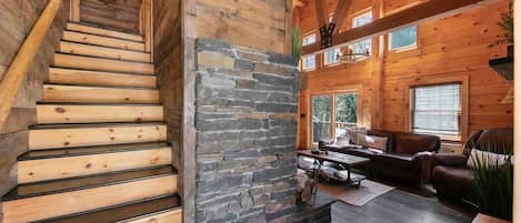A wooden interior with a staircase, stone wall, and a living area with a sofa and coffee table.