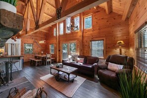 Ein geräumiges Blockhaus-Interieur mit Essbereich, einem Wohnzimmer mit Sofa und Sesseln sowie großen Fenstern für viel Tageslicht.