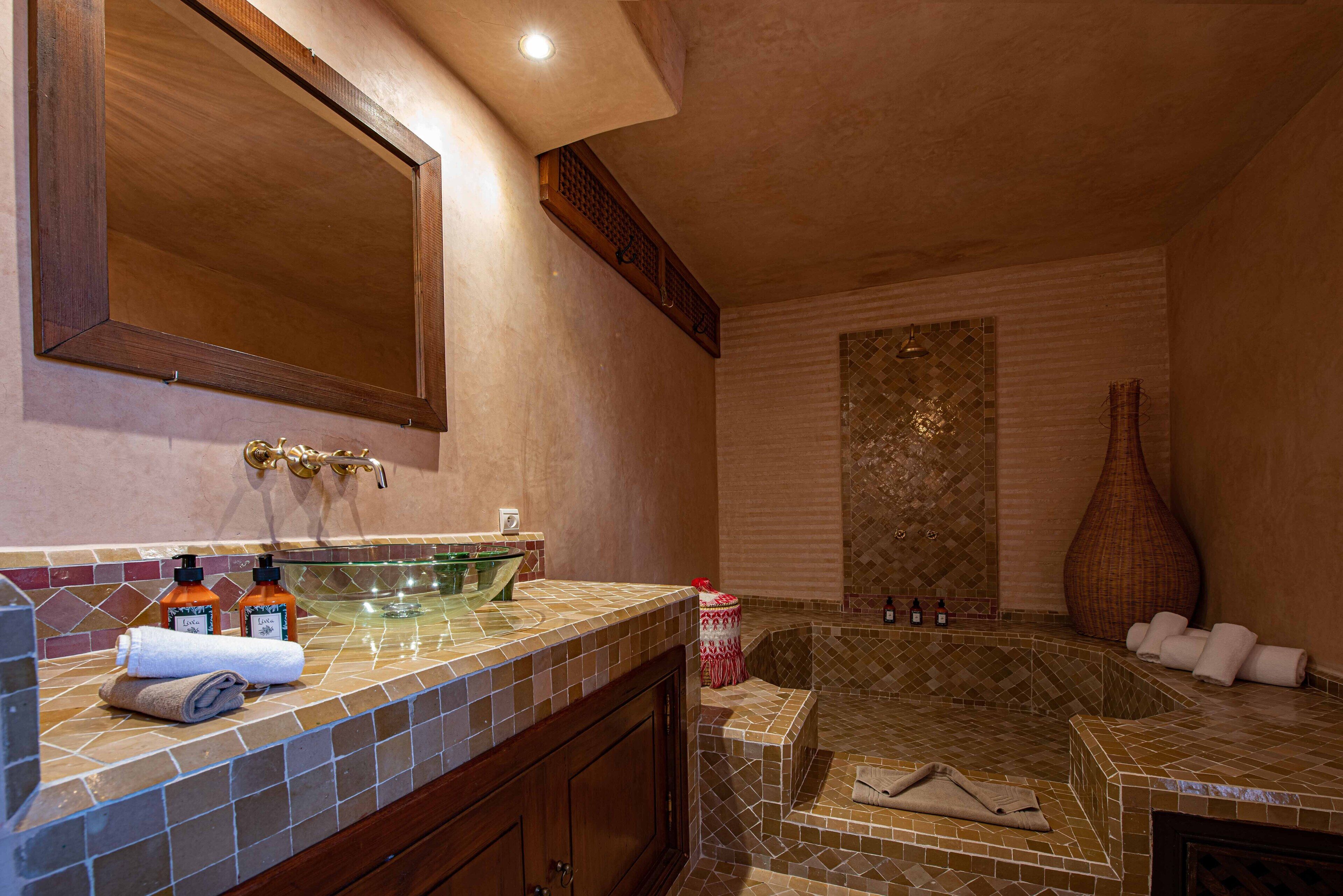 A bathroom with a large mirror, a glass sink, a bathtub, and a tiled floor.