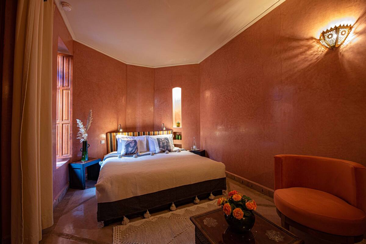 A bedroom with a large bed, a nightstand, a chair, and a vase with flowers.