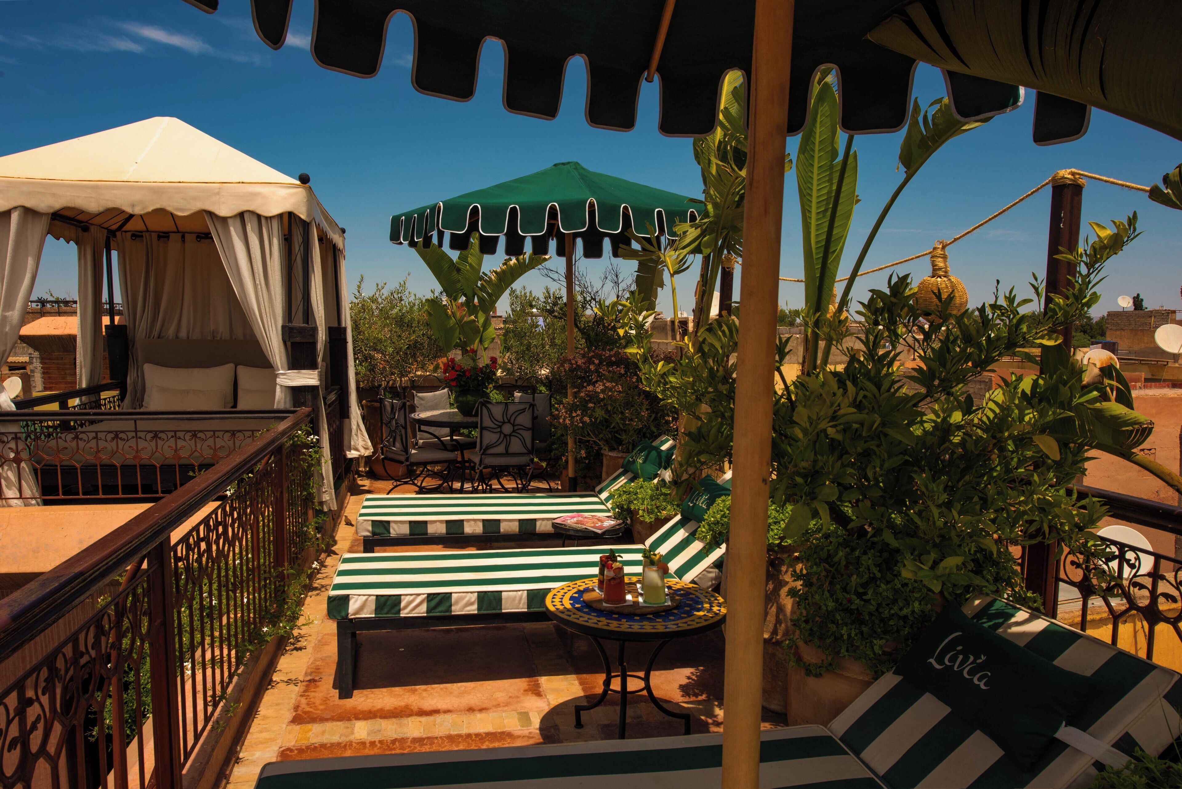 A rooftop terrace with a canopy, striped seating, a table with drinks, and a tent.