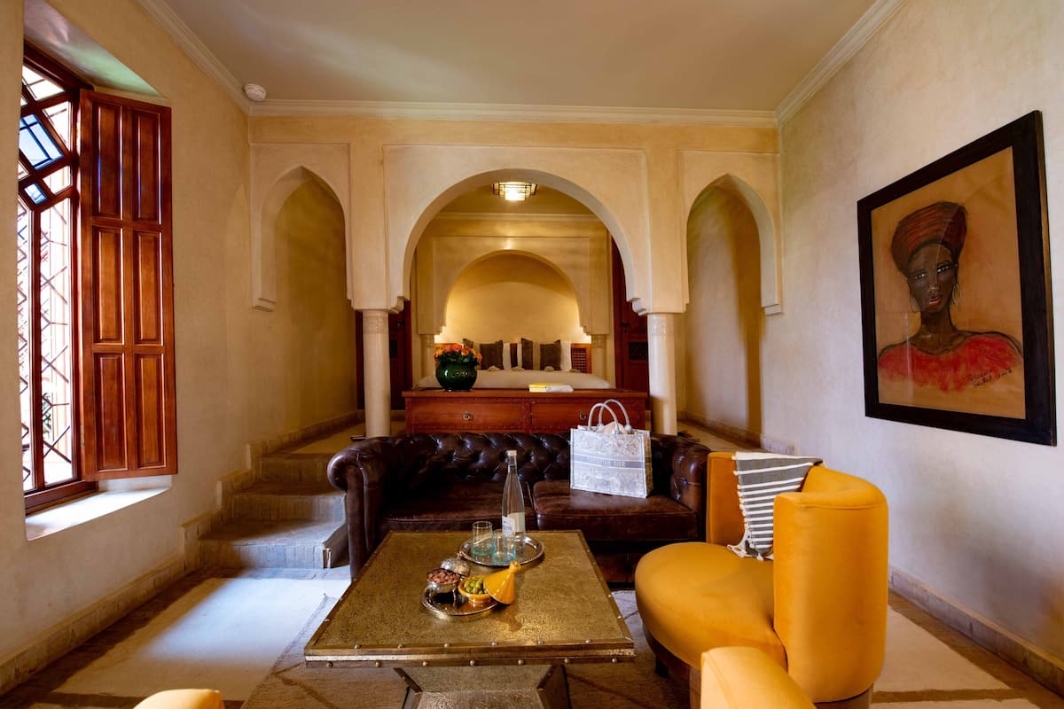 A lobby with a brown leather sofa, a yellow armchair, a coffee table with a tray, and a framed painting on the wall.