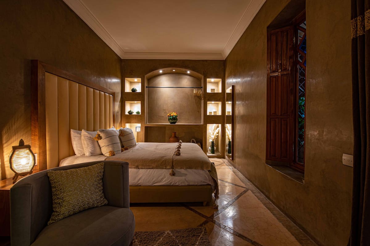 A bedroom with a large bed, bedside tables, a nightstand, a sofa, and a decorative vase.