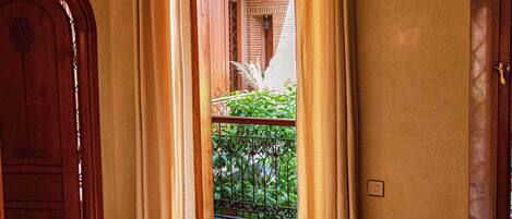 Une pièce avec une porte en bois, un fauteuil jaune, une table avec une théière et des tasses, et une vue sur un balcon orné de plantes.