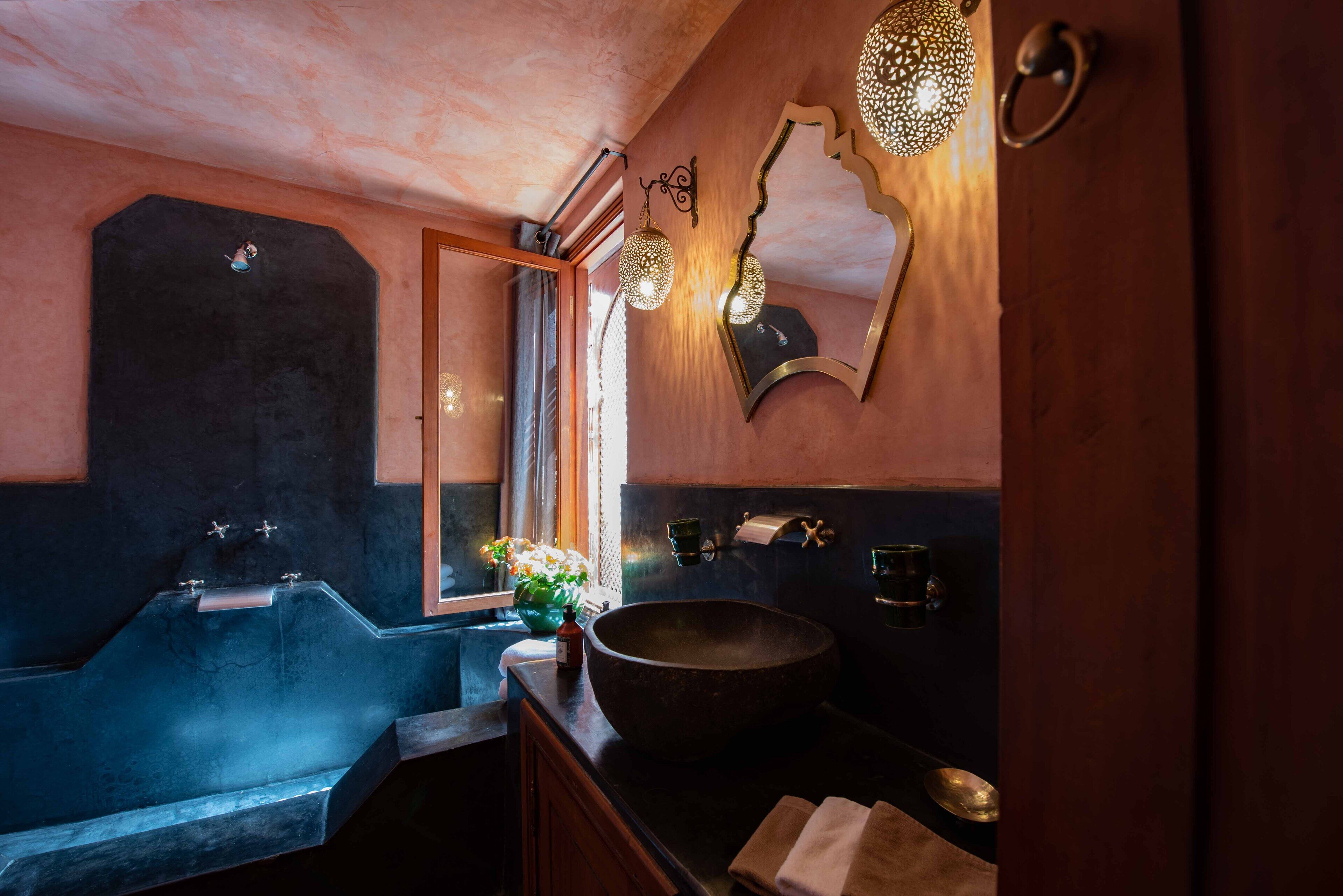 Un baño con una bañera grande, un lavabo redondo y un espejo de diseño único.
