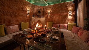 Uma sala de jantar com uma mesa comprida posta para refeição, cercada por assentos acolchoados.