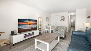 Ein Wohnzimmer mit Fernseher, weißen Möbeln, einem gemusterten Sessel und einem blauen Sofa.