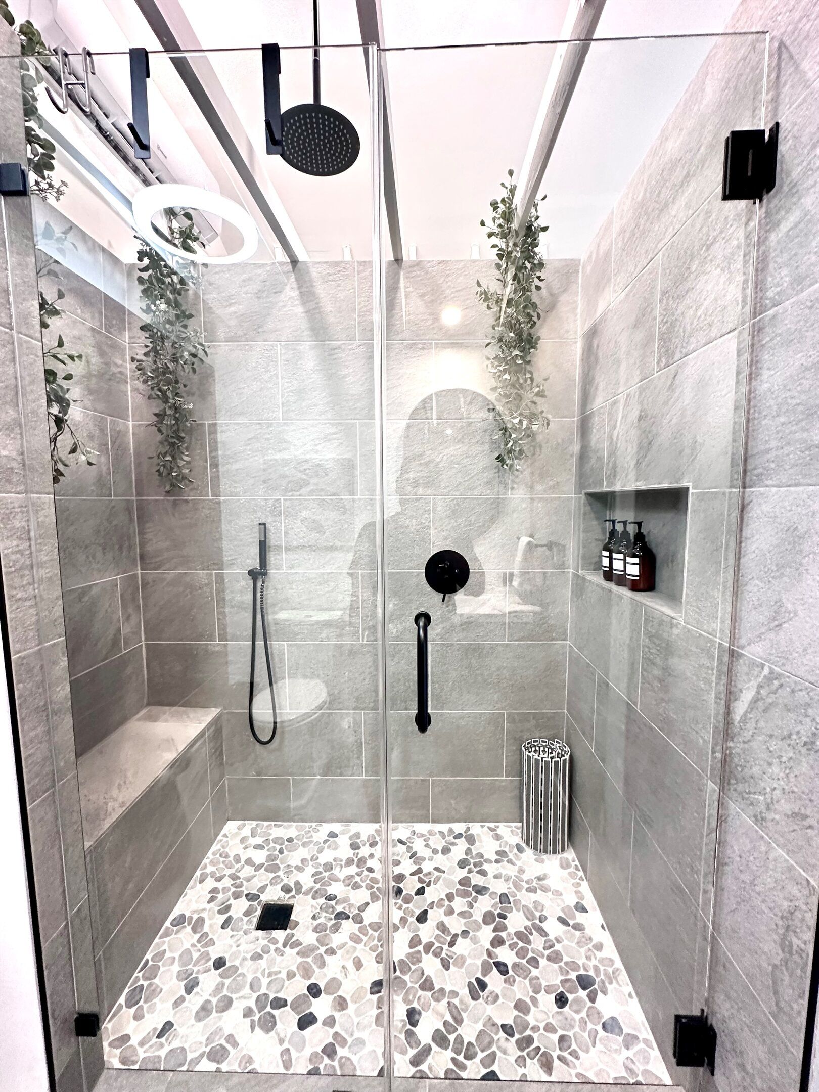 A modern shower with a glass door, stone tiles, and a built-in shelf with toiletries.