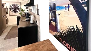 Cocina moderna con encimera de madera, una isla negra y un cuadro grande con una escena de playa.