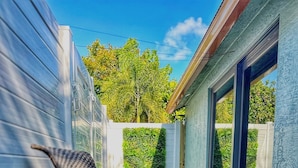 Un patio con una pequeña mesa y sillas, un arreglo floral y vista a un jardín verde con árboles.