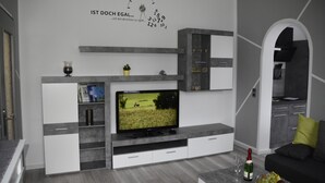 Uma sala de estar moderna com televisão de tela plana, estantes embutidas, uma taça de vinho e uma fruteira.