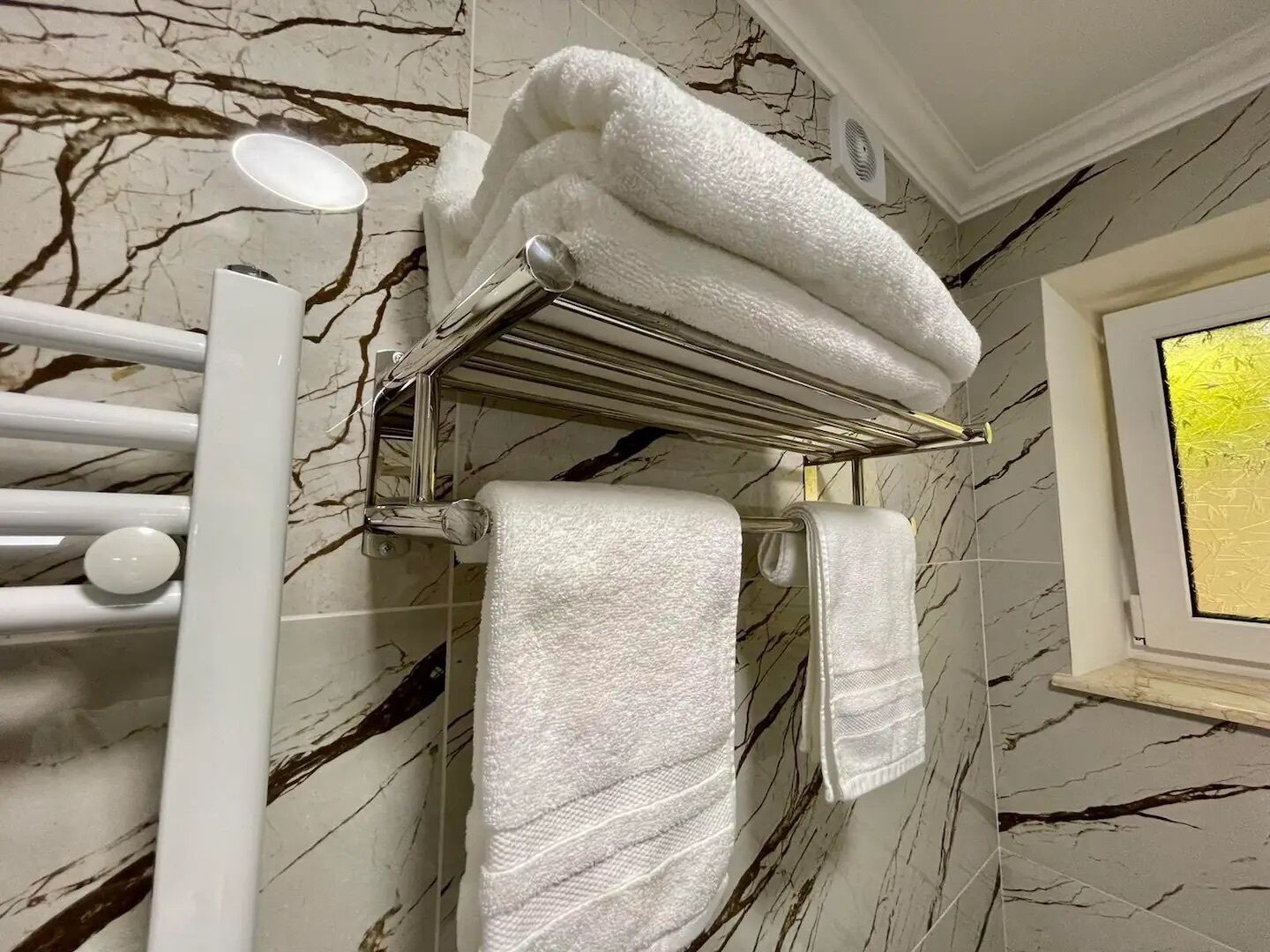A bathroom with marble walls, a towel rack with folded towels, and a window with a view.