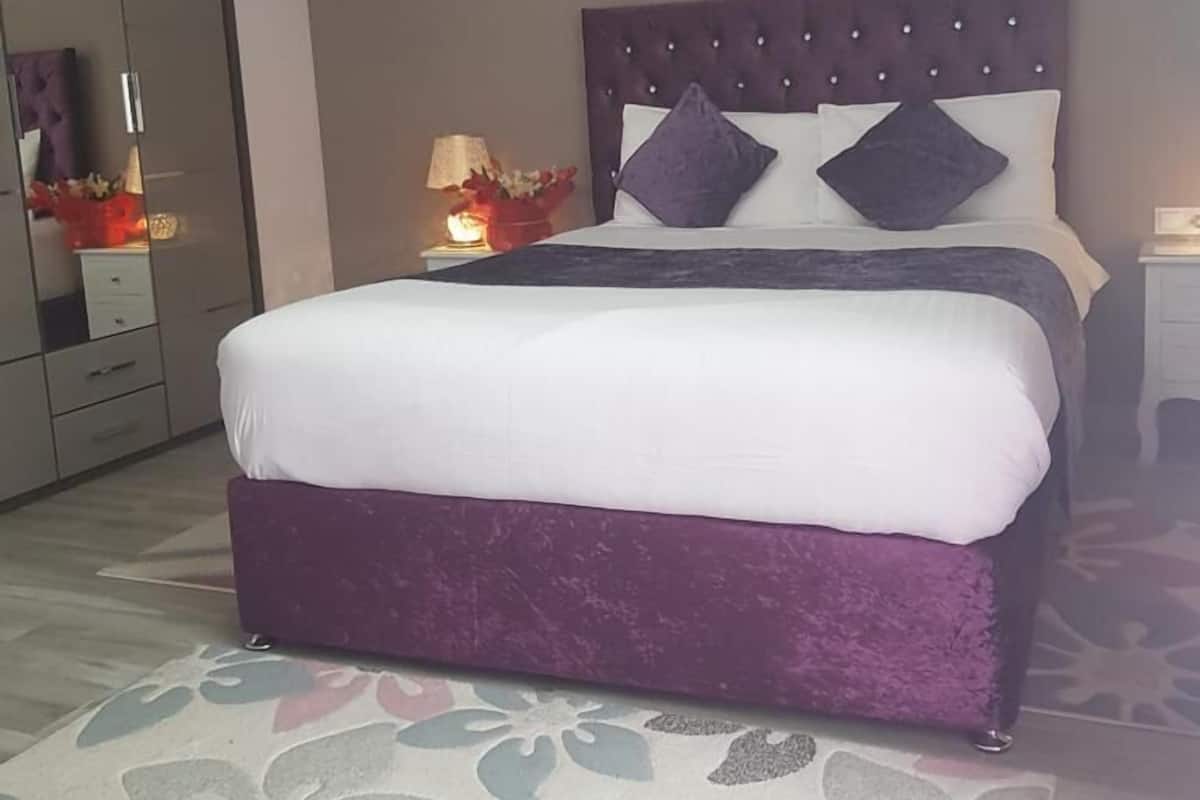Een moderne slaapkamer met een groot bed, een nachtkastje met een lamp en een spiegel.